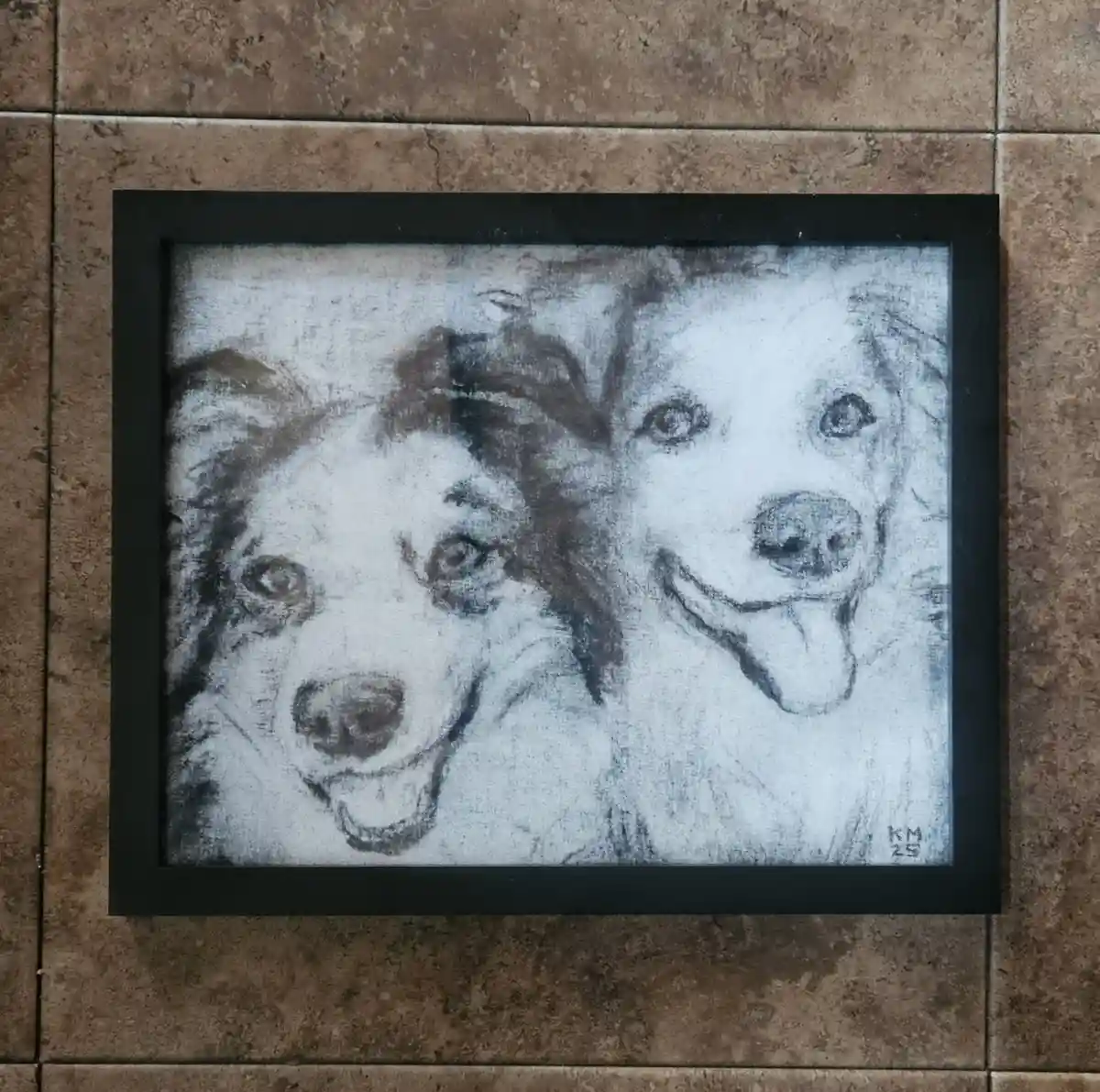A framed black-and-white chalk drawing on a tiled wall shows two happy-looking dogs with tongues out. The artwork is signed…