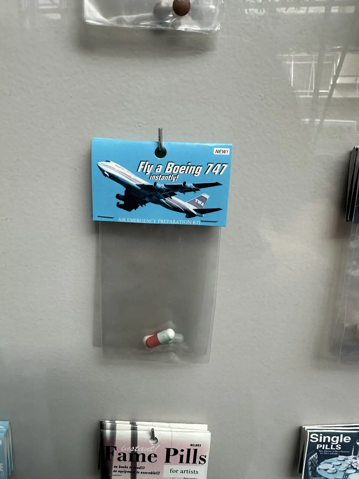A product package labeled 'Fly a Boeing 747 instantly! AIR EMERGENCY PREPARATION KIT' contains a single red-and-white pill…