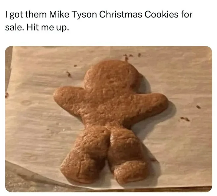 A plain, unadorned gingerbread man cookie sits on parchment paper, its shape resembling a human figure with a rounded head…