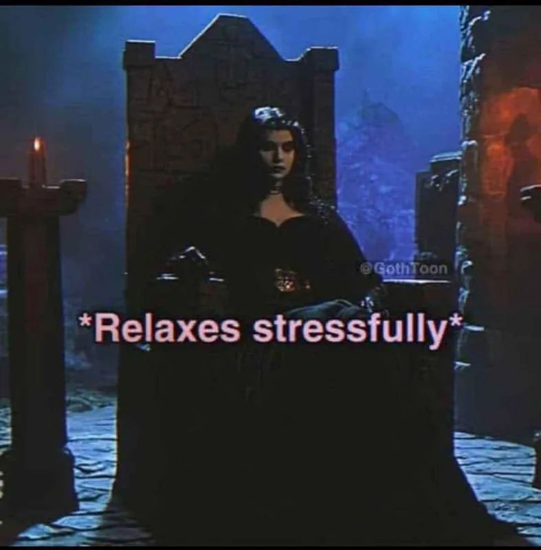 A woman with dark hair and gothic attire sits regally on a stone throne in a dimly lit, dungeon-like room with blue and…