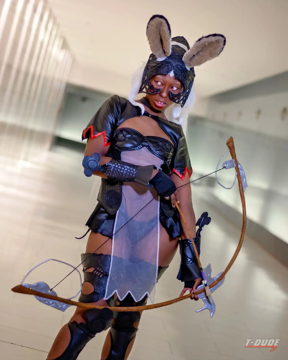 A person in a detailed cosplay of a rabbit-themed archer character, wearing a black leather outfit with bunny ears, holding…