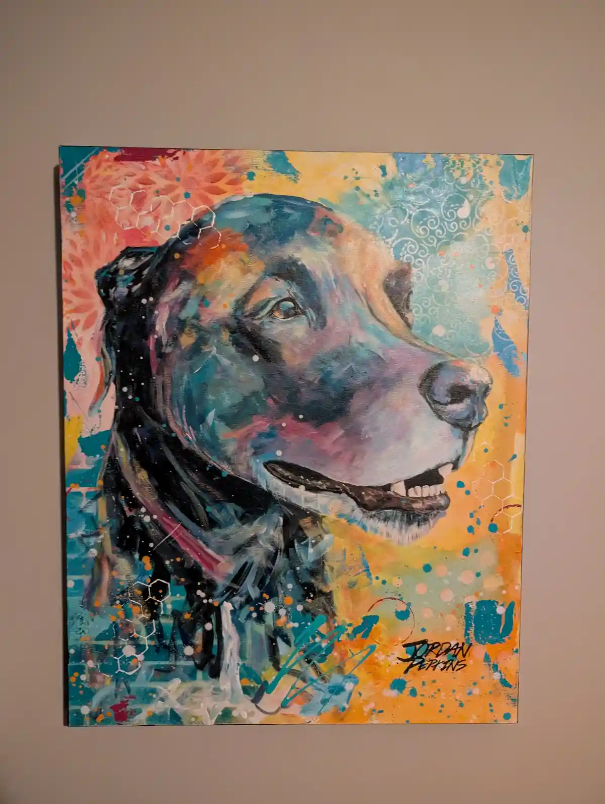 A colorful abstract painting of a dog's head in profile, hanging on a beige wall. The artwork features vibrant splashes of…