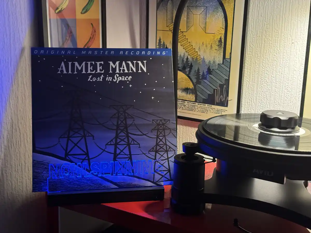 A vinyl record player with a record on it sits next to the album cover for Aimee Mann's 'Lost in Space'. The album cover…