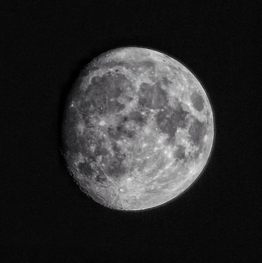 A high-resolution black and white photograph of the full moon against a dark sky, showing detailed craters and surface…