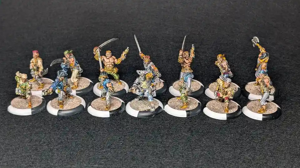 A row of ten hand-painted miniature pirate figurines, each on a circular base with sand texture, posed dynamically with…