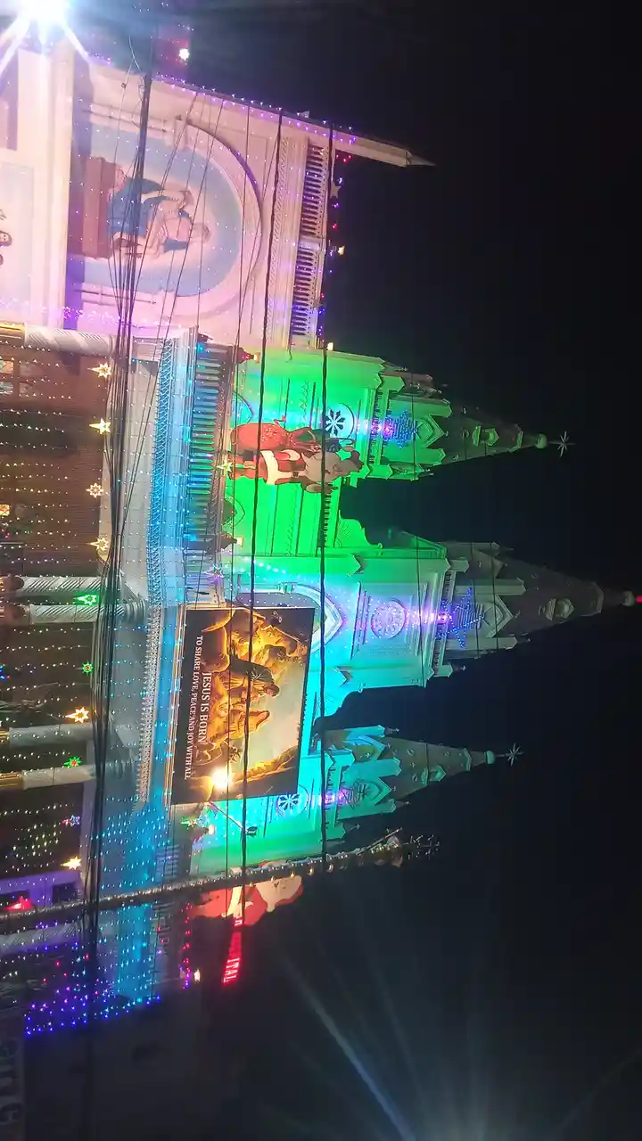 A nighttime photo of a church heavily decorated with colorful Christmas lights and festive ornaments, including large Santa…