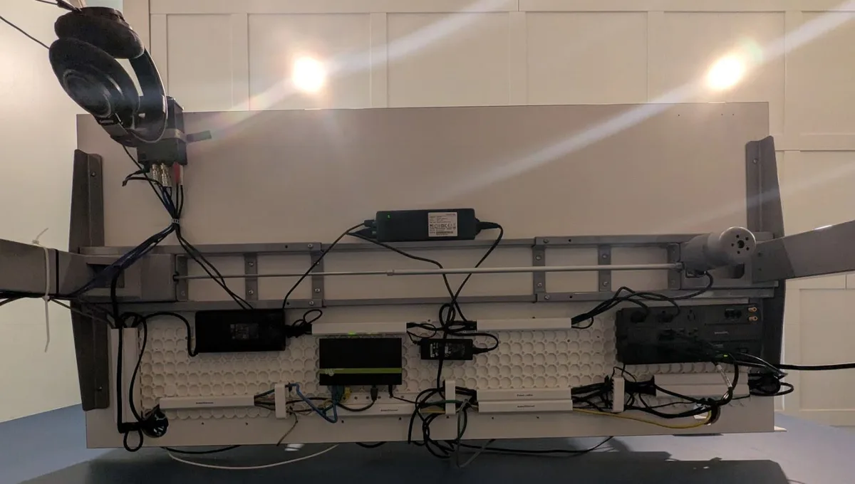 The image shows the back of a large monitor or screen setup with a tangle of wires, multiple power adapters, a gaming…