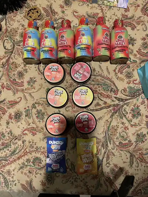 Six colorful bottles of Uncle Arnies cannabis-infused beverages and six round containers of Happy Fruit gummies are arranged…