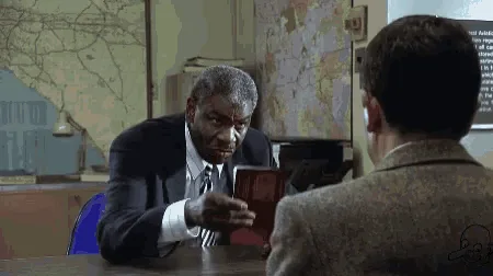 A composite image showing Mr. Bean in a passport office, visibly reacting with escalating shock and horror as he looks at…