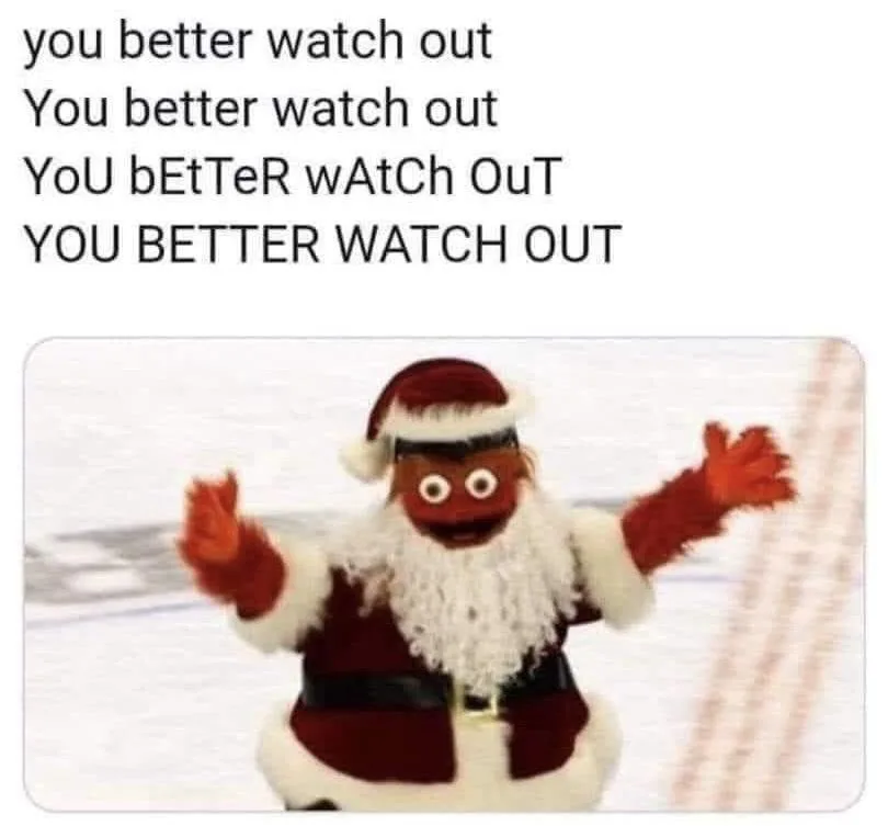 A photo of a puppet dressed as Santa Claus with a white beard, red hat, and red suit, arms outstretched against a snowy…