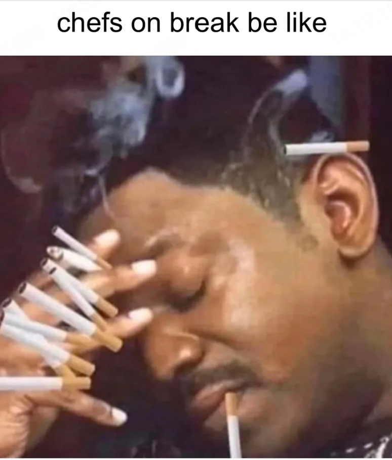 A man with his eyes closed and multiple cigarettes stuck in his fingers, ear, and mouth, with smoke rising around him. The…