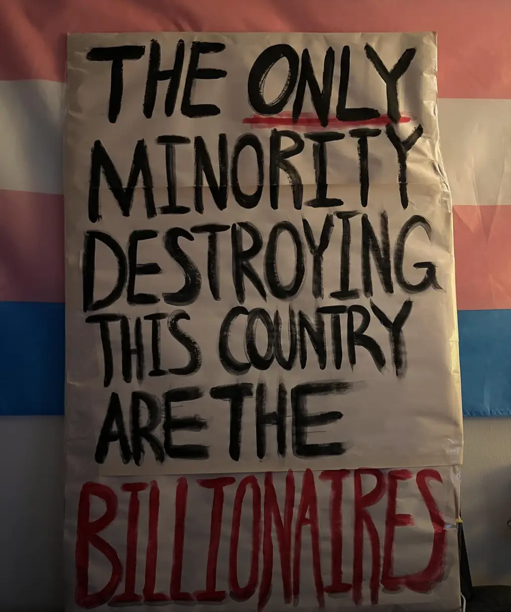 A handmade protest sign with bold black and red handwritten text on white paper, stating 'THE ONLY MINORITY DESTROYING THIS…