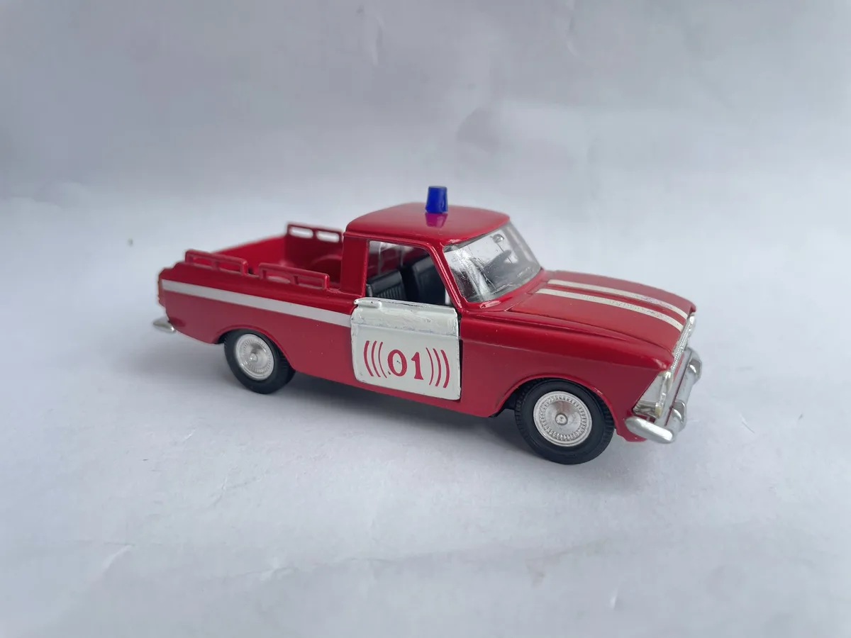 A red toy pickup truck with a blue light on top and white stripes, shown against a plain white background. The side door has…