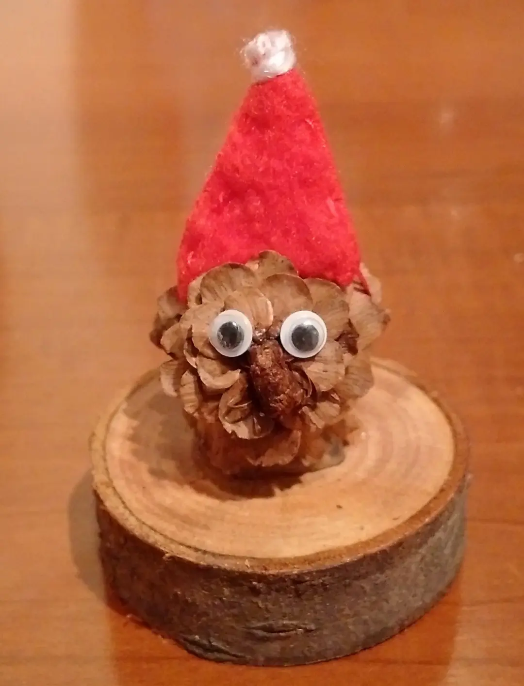 A small pinecone with googly eyes and a red felt Santa hat sits atop a wooden slice, with the overlaid text reading 'i'm not…