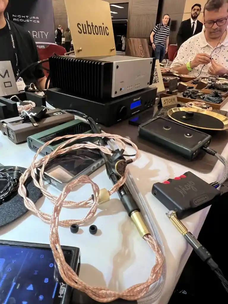 A photo of a high-end audio equipment table at an expo, featuring a large silver and black amplifier labeled 'subtonic' on a…
