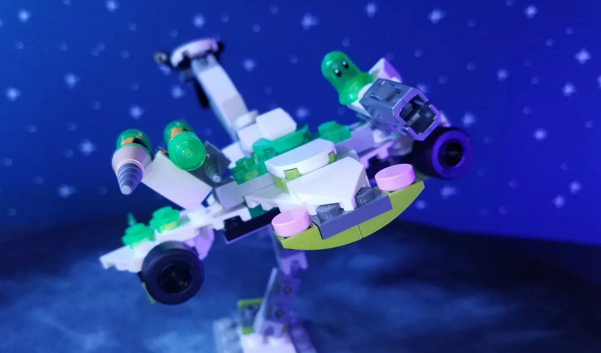 A custom-built LEGO spaceship, primarily white, green, and purple, is posed against a starry blue background. The ship…