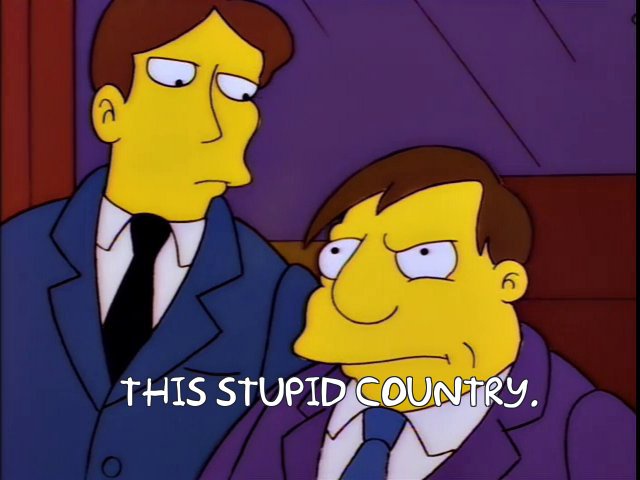 Two yellow-skinned cartoon men in suits sit side by side; the man on the right, with a smug expression, has the text 'THIS…