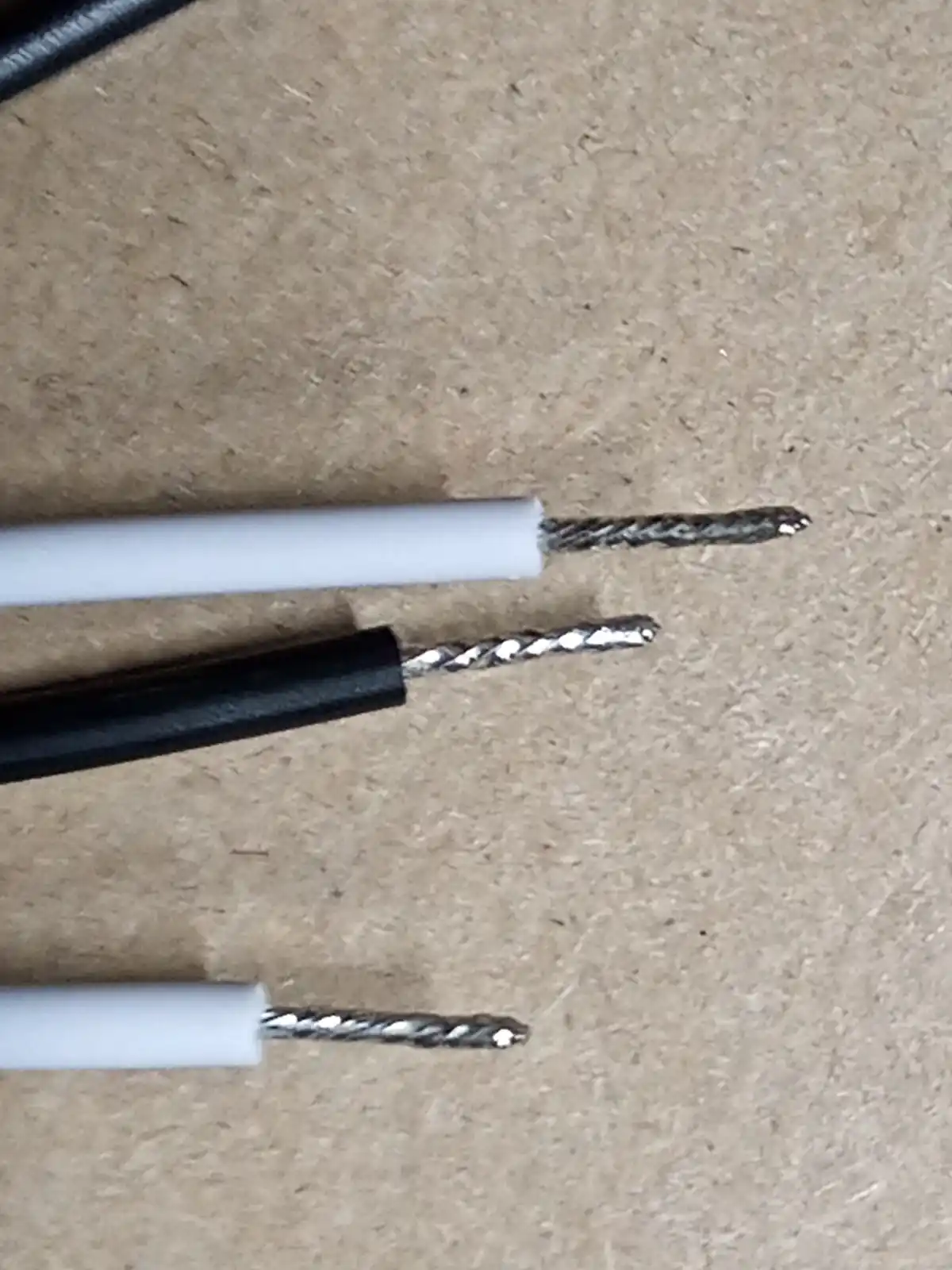 Three wires with stripped ends lie on a brown textured surface, their exposed metal tips resembling drill bits. The overlaid…