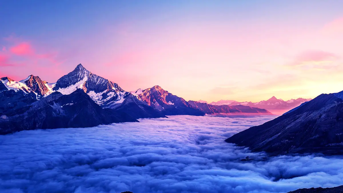 A breathtaking mountain landscape at sunrise or sunset, featuring snow-capped peaks rising above a sea of clouds. The sky is…