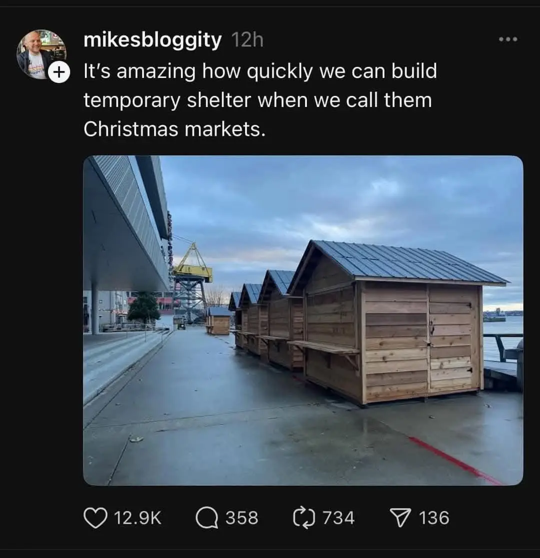 A social media post by 'mikesbloggity' shows a row of small, wooden, temporary market stalls with metal roofs set up on a…