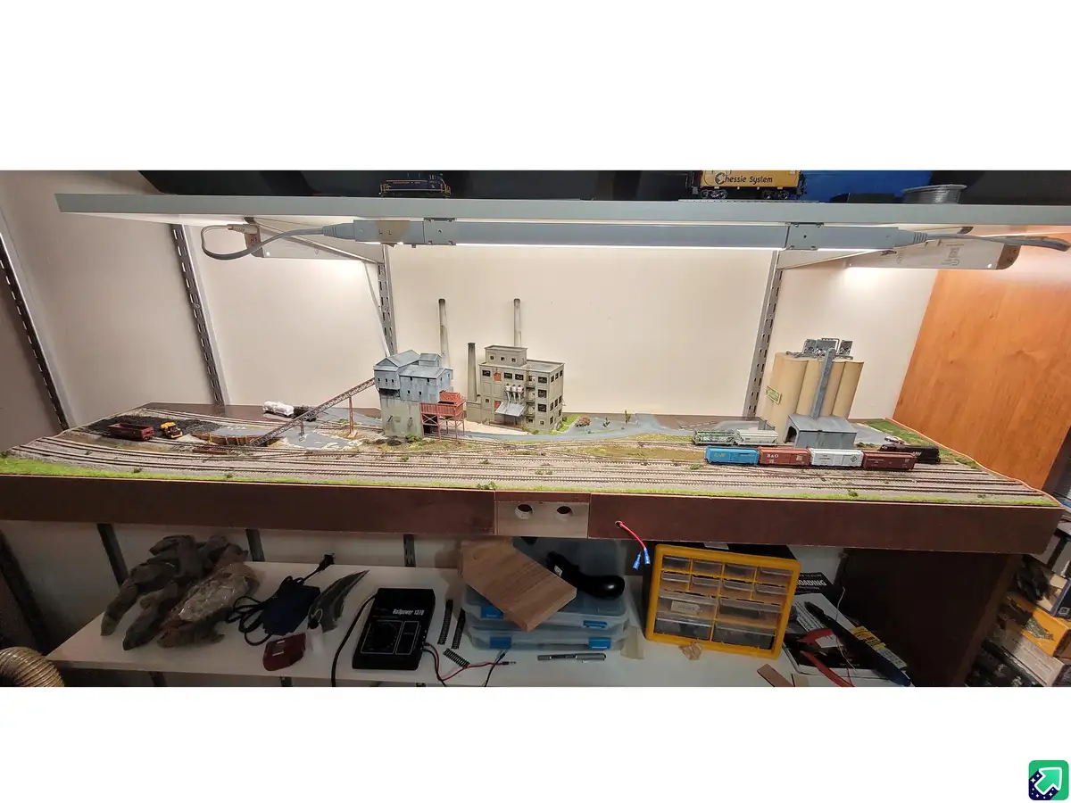 A detailed model railroad layout sits on a shelf under a light, featuring miniature buildings, tracks, and trains, with…
