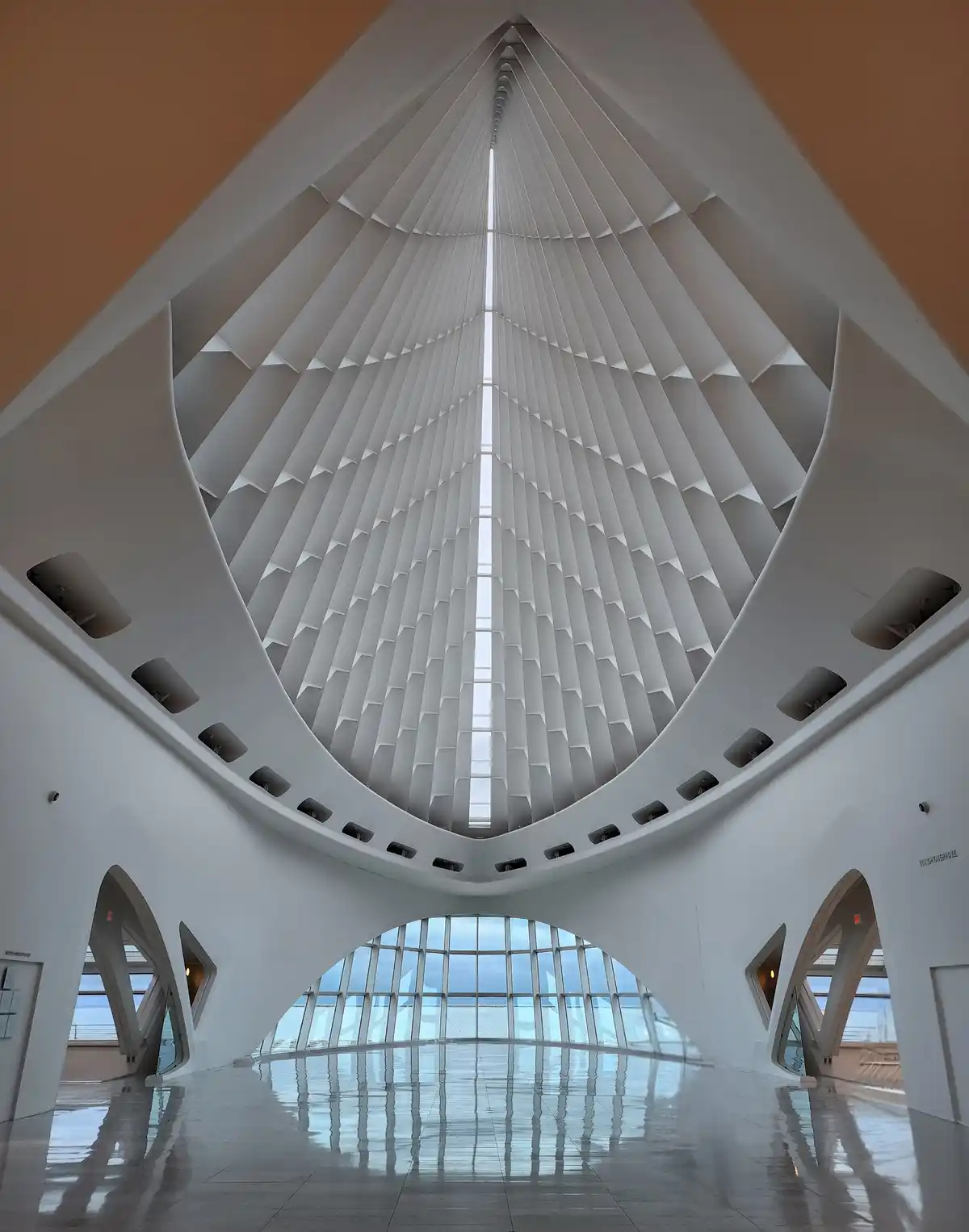 A low-angle shot captures the soaring, white, geometrically patterned ceiling of a modern architectural space, likely the…