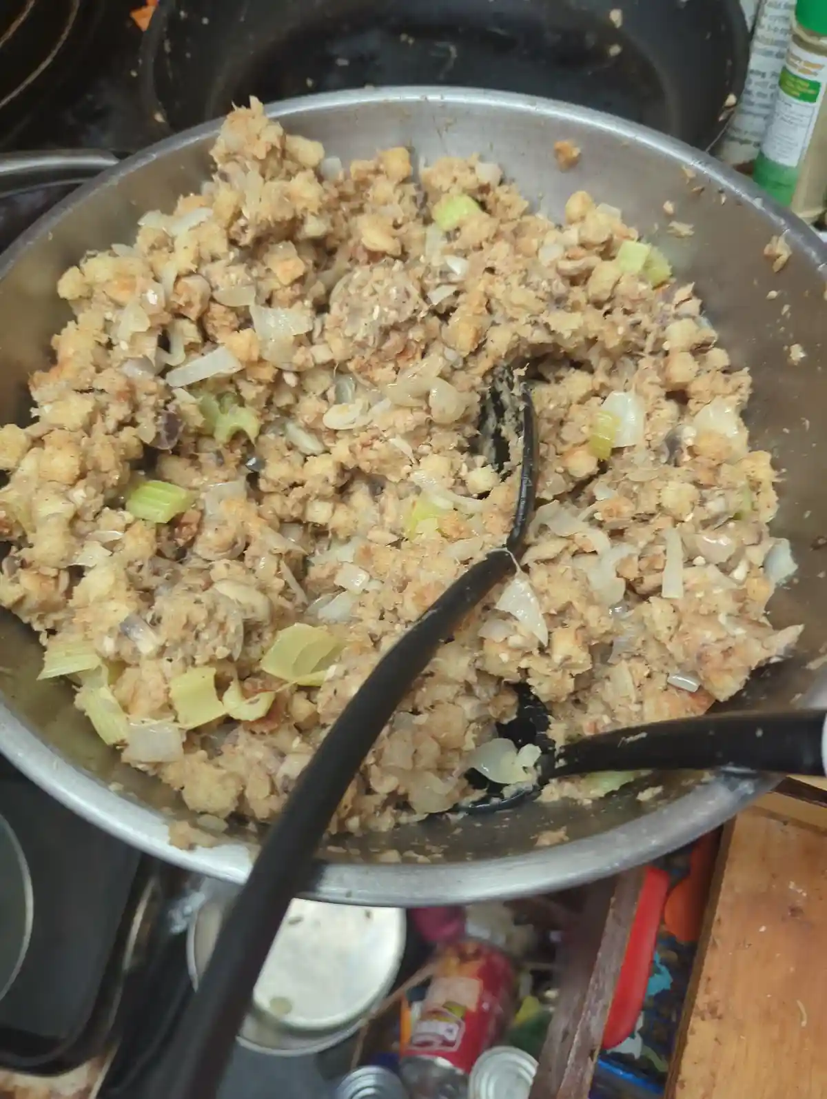 A close-up photo shows a large metal mixing bowl filled with homemade stuffing, visibly containing crumbled bread, chopped…