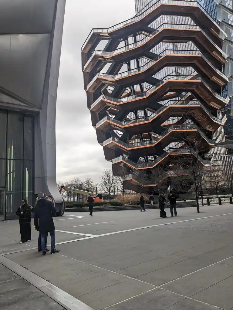 The image shows the Vessel public art installation in Hudson Yards, New York City, a distinctive copper-colored…