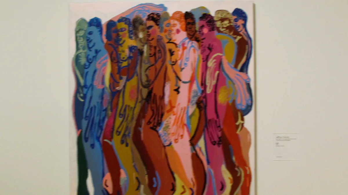 A colorful, abstract painting of multiple stylized human figures in various poses and hues hangs on a white wall in what…