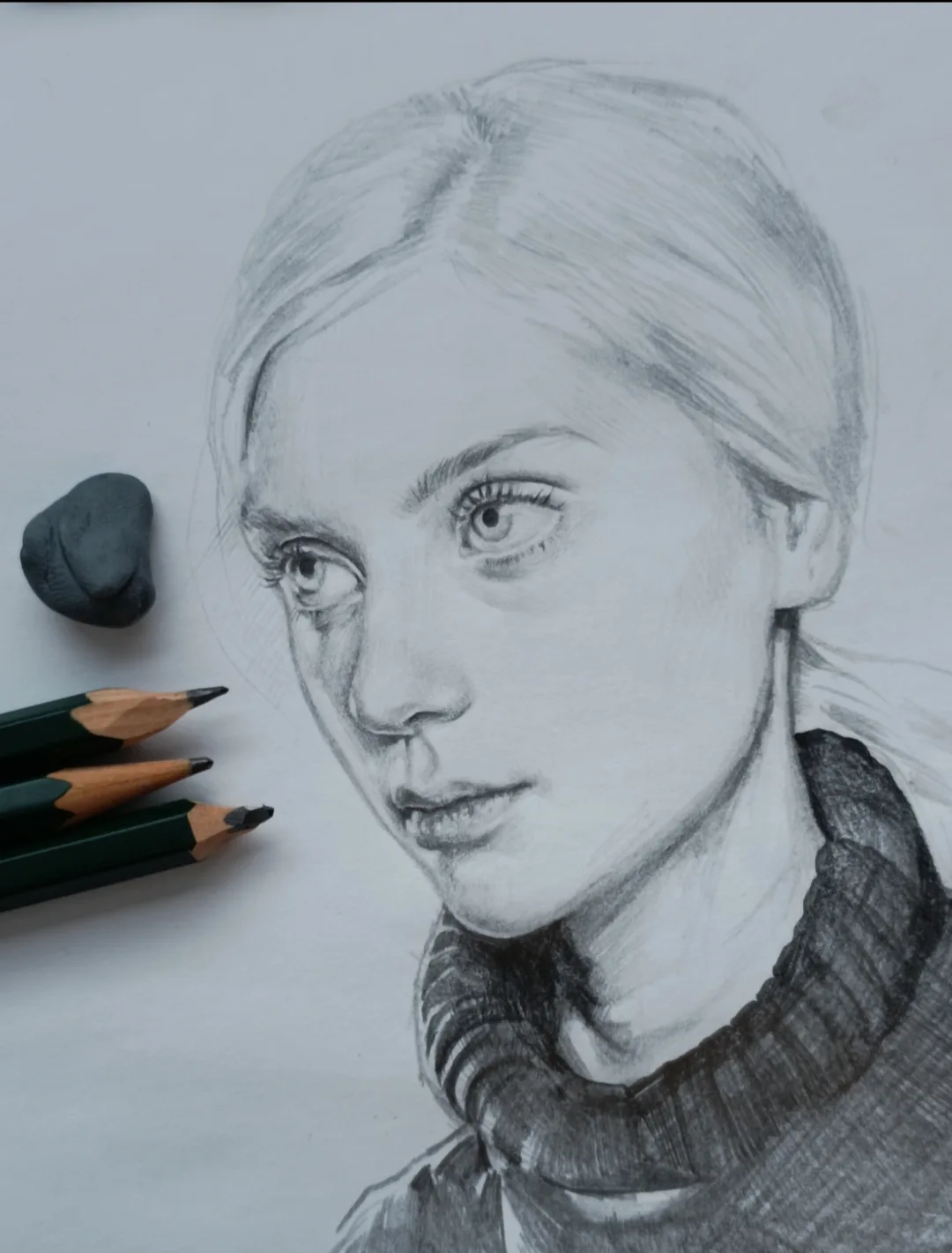 A detailed pencil sketch of a young woman with blonde hair and a high-neck sweater, rendered on white paper. To the left…