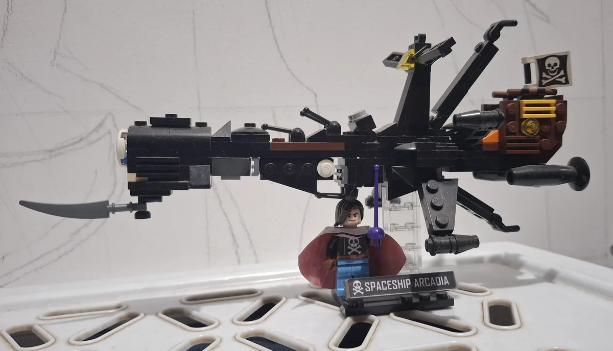 A LEGO pirate spaceship model named 'SPACESHIP ARCADIA' with a skull and crossbones flag, featuring a minifigure captain in…