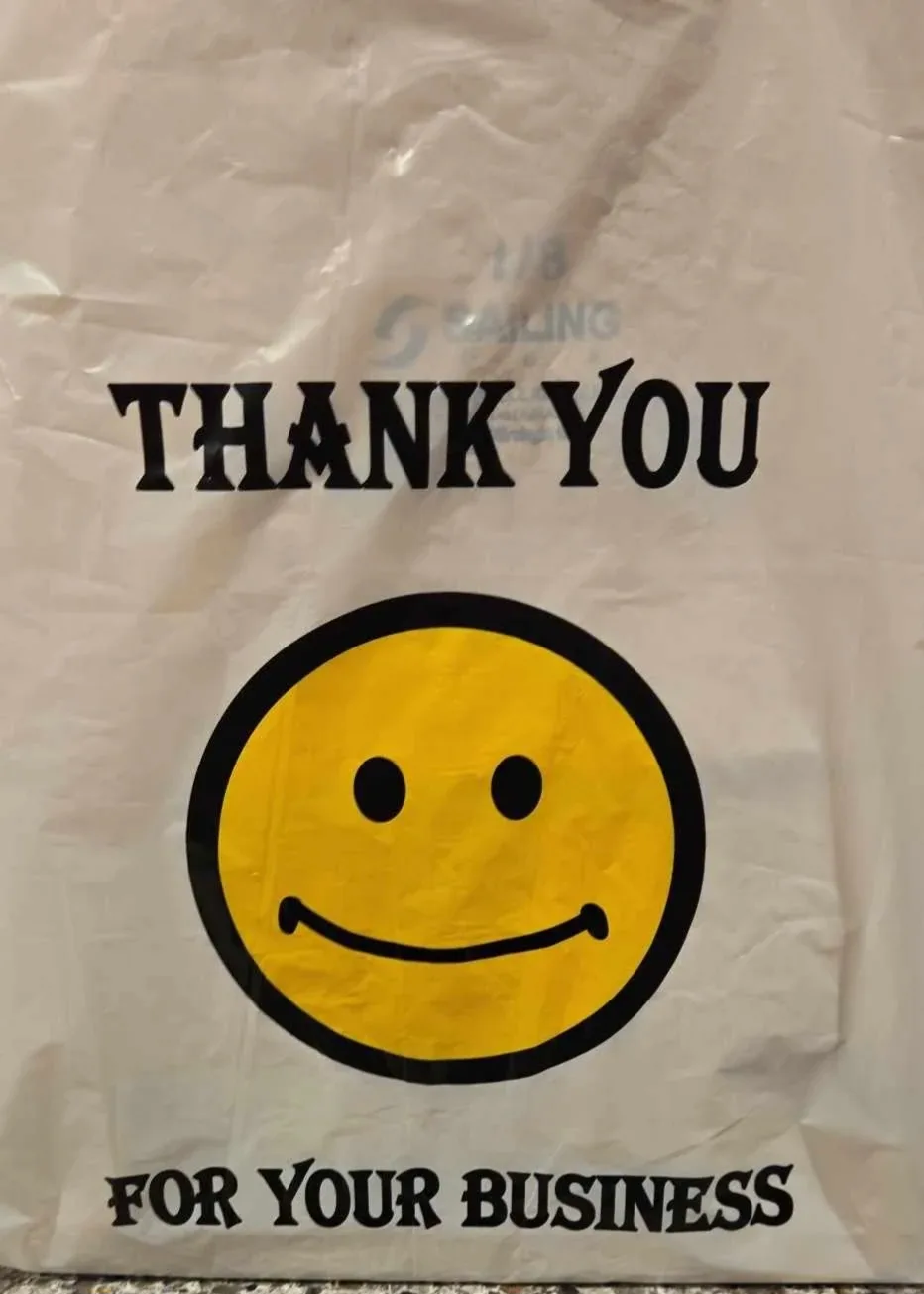 A crumpled white plastic bag with a large yellow smiley face and the text 'THANK YOU FOR YOUR BUSINESS' printed in bold…