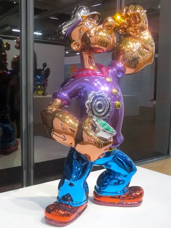 A shiny, multi-colored statue of a cartoon character resembling Mickey Mouse, with metallic purple torso, blue pants, and…