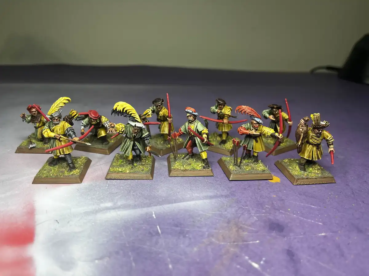 A row of hand-painted miniature figurines, dressed in historical-style yellow and green uniforms with feathered hats, are…