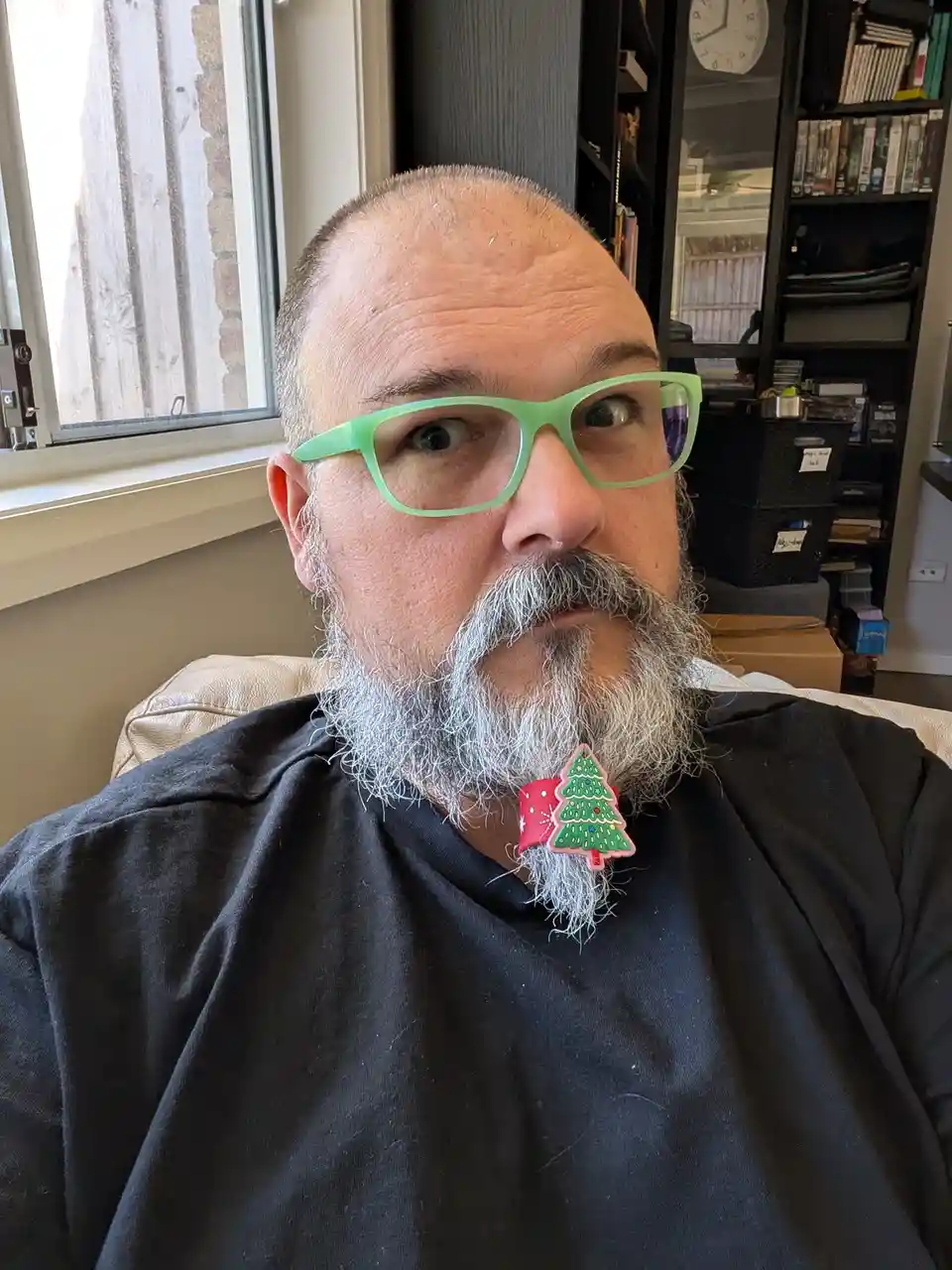 A man with a gray beard and green glasses stares directly at the camera with a surprised expression. A small, colorful…
