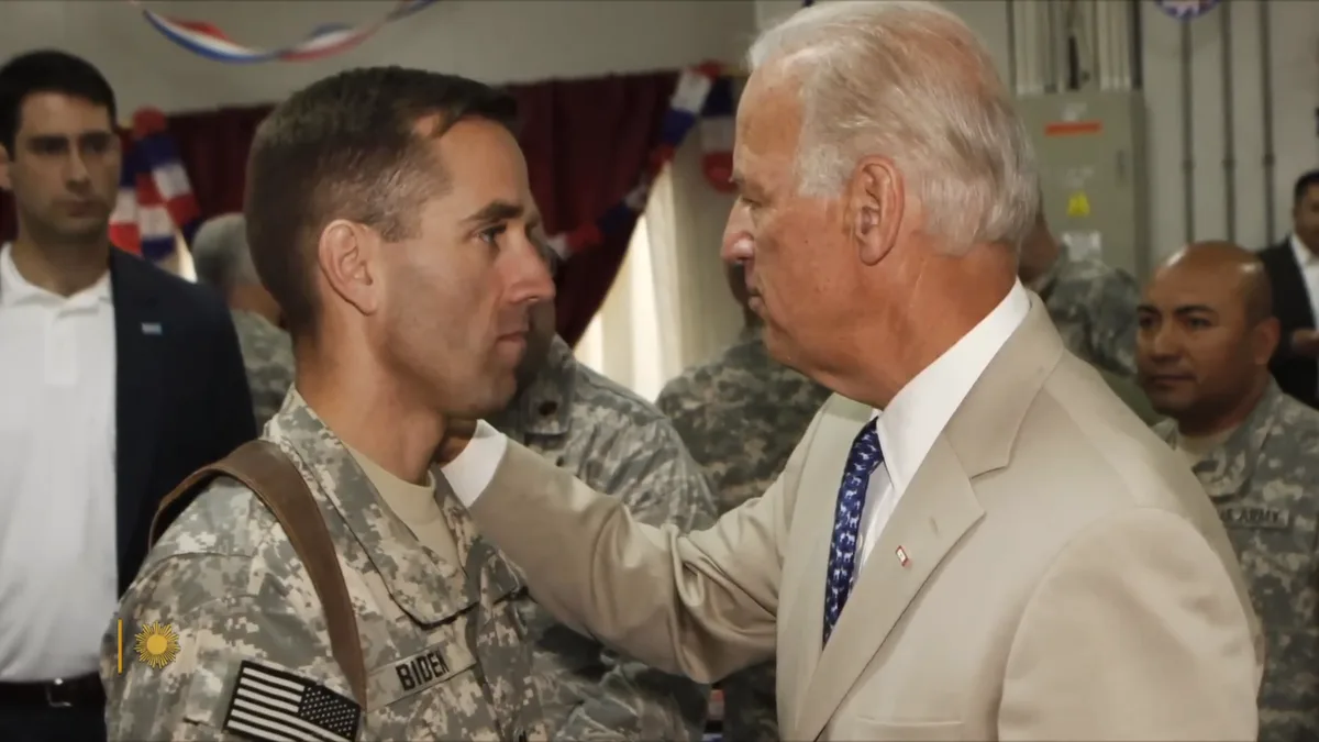 An older man in a beige suit places his hand on the shoulder of a younger man in a U.S. Army uniform with 'BIDEN' on his…
