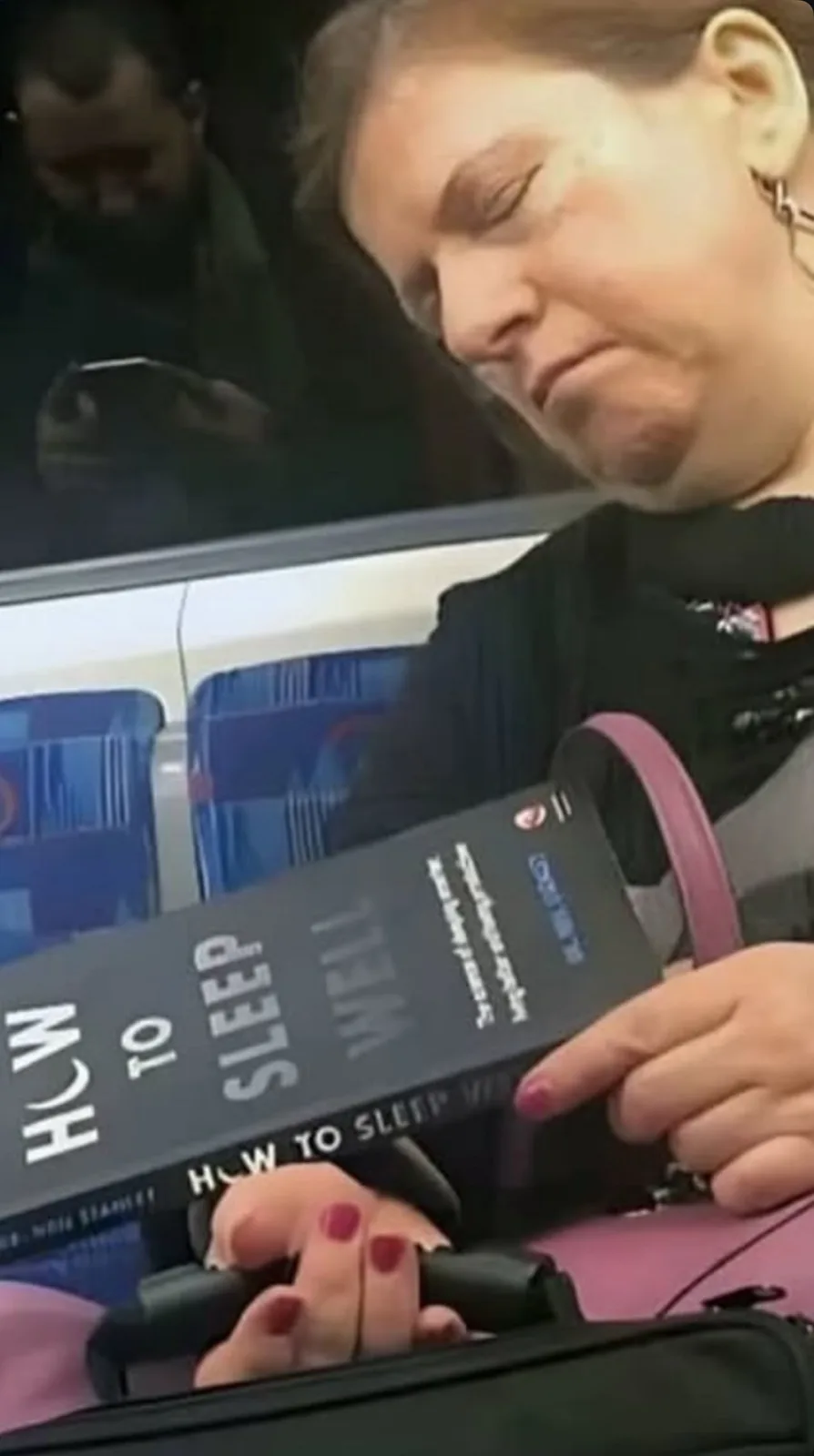 A woman is asleep on public transport, holding a book titled 'How to Sleep Well' by Dr. Neil Stanley. Her eyes are closed…
