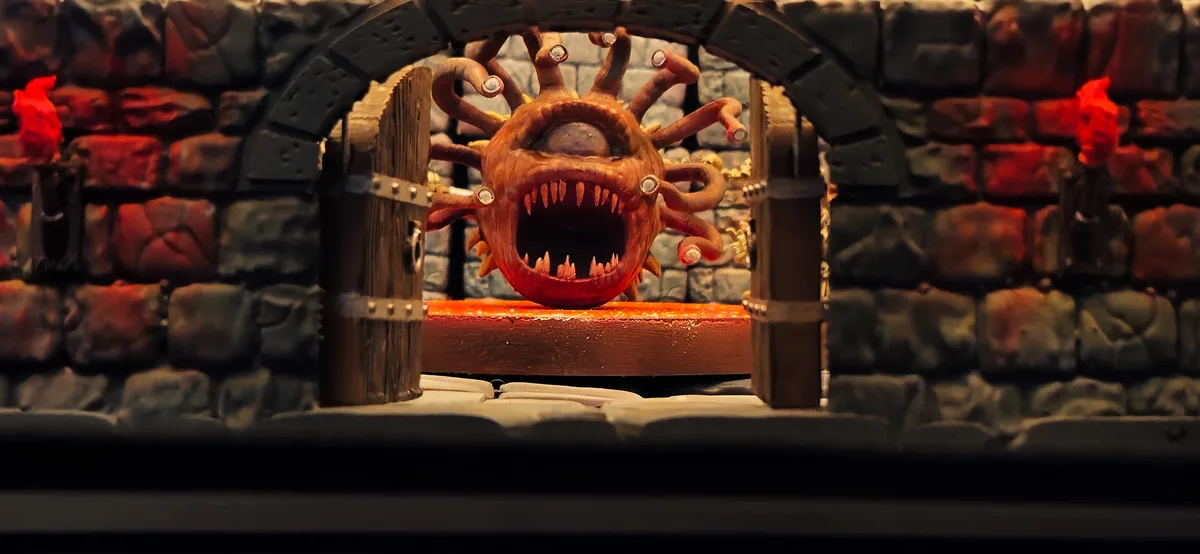 A close-up of a grotesque, orange, multi-limbed monster with a wide, toothy grin and glowing eyes, emerging from behind a…