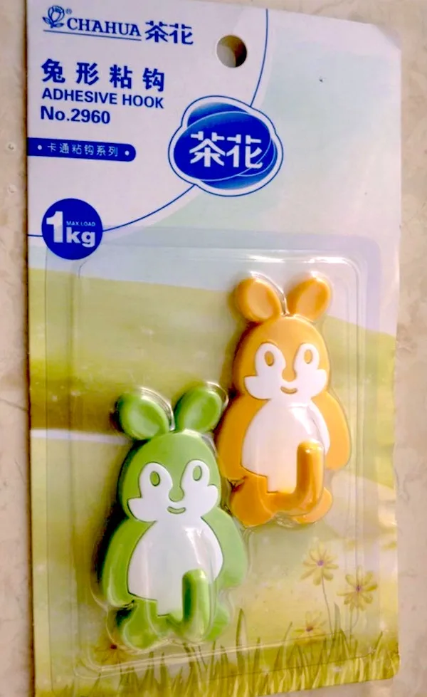 A package of two cartoon rabbit-shaped adhesive hooks, one green and one yellow, shown in their plastic blister pack. The…
