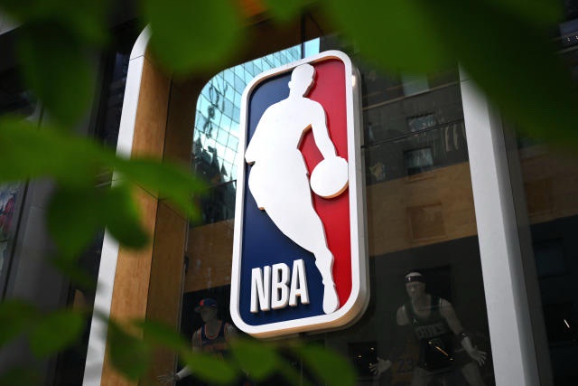 A large, illuminated NBA logo sign featuring a white silhouette of a basketball player dribbling against a red and blue…
