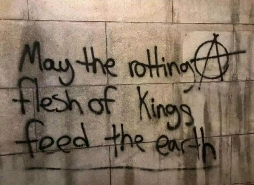 Handwritten graffiti on a tiled wall reads 'May the rotting flesh of Kings feed the earth,' with the letter 'A' in 'rotting'…