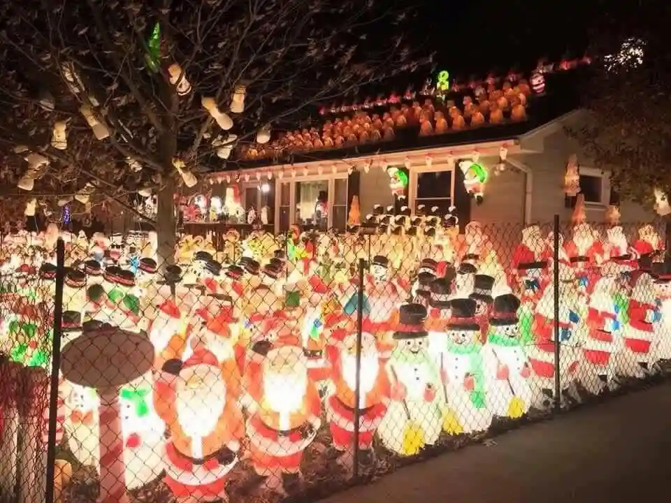 A nighttime photo of a house and yard covered in hundreds of illuminated, plastic Christmas decorations, primarily snowmen…