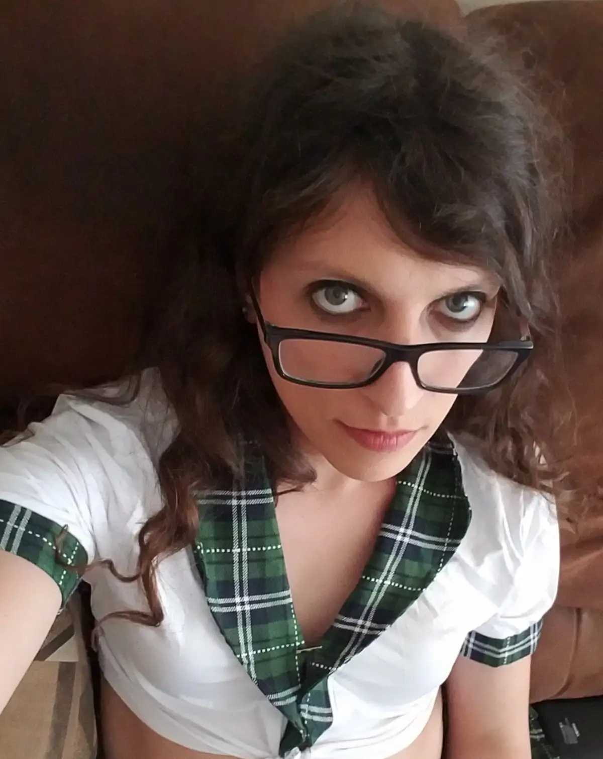 A person with dark curly hair and black-rimmed glasses stares intensely at the camera while wearing a white shirt with a…