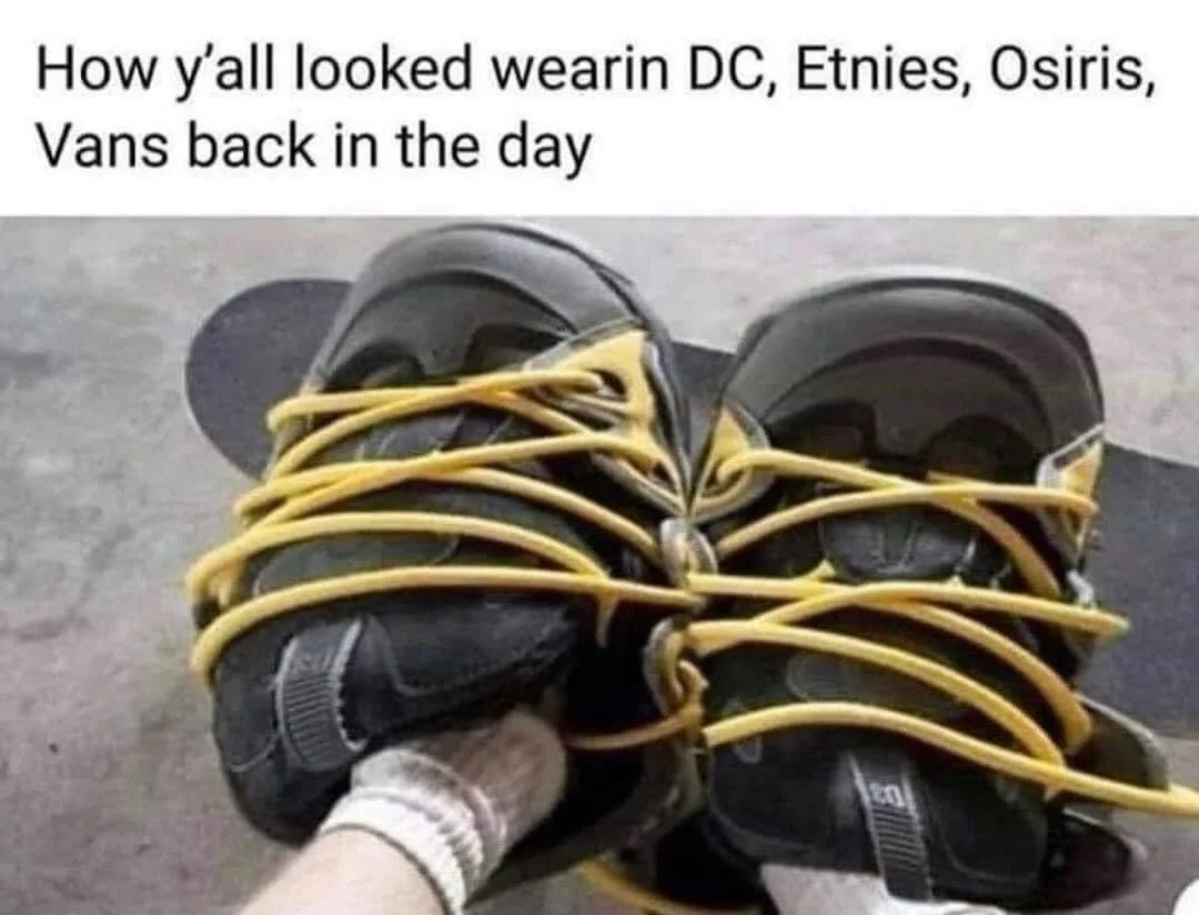 A pair of black skate shoes with bright yellow laces are tied together in a messy, tangled knot, resting on a skateboard…