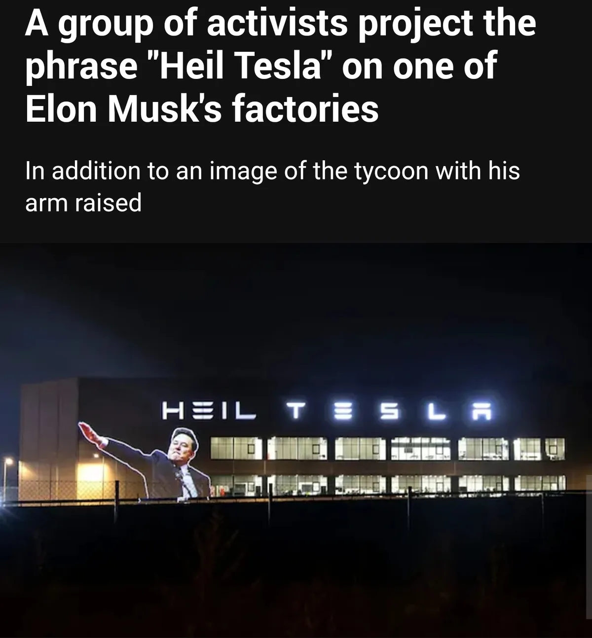 A nighttime photo shows a large projection on the side of a factory building. The projection displays the text "HEIL TESLA"…