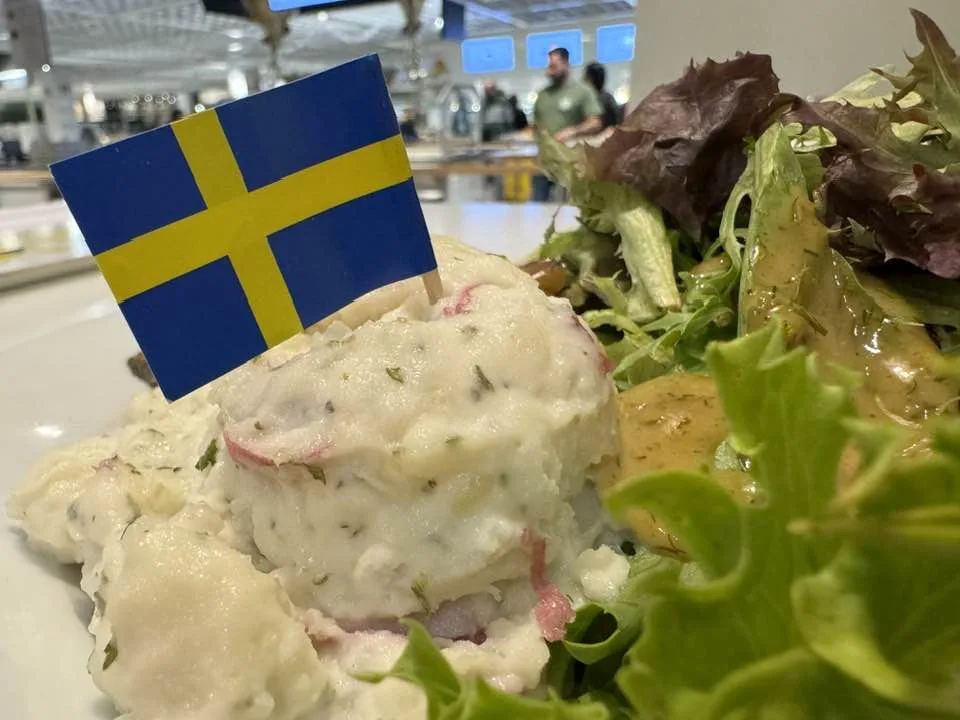 A close-up photo of a plate of mashed potatoes with visible herbs and thin slices of red potato, garnished with a small…