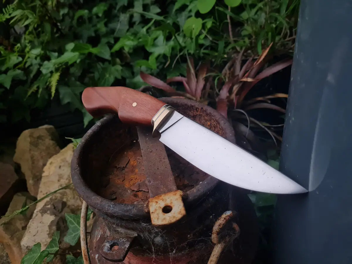 A shiny, clean knife with a wooden handle rests inside a rusty, weathered metal container, its blade touching a dark…