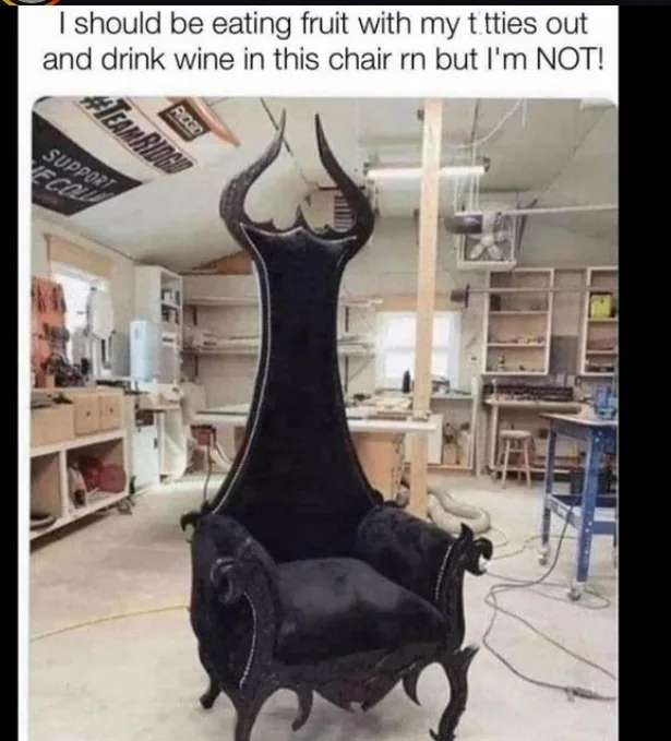 A black, ornate, high-backed throne-like chair with curved horns sits in a cluttered workshop filled with tools, shelves…