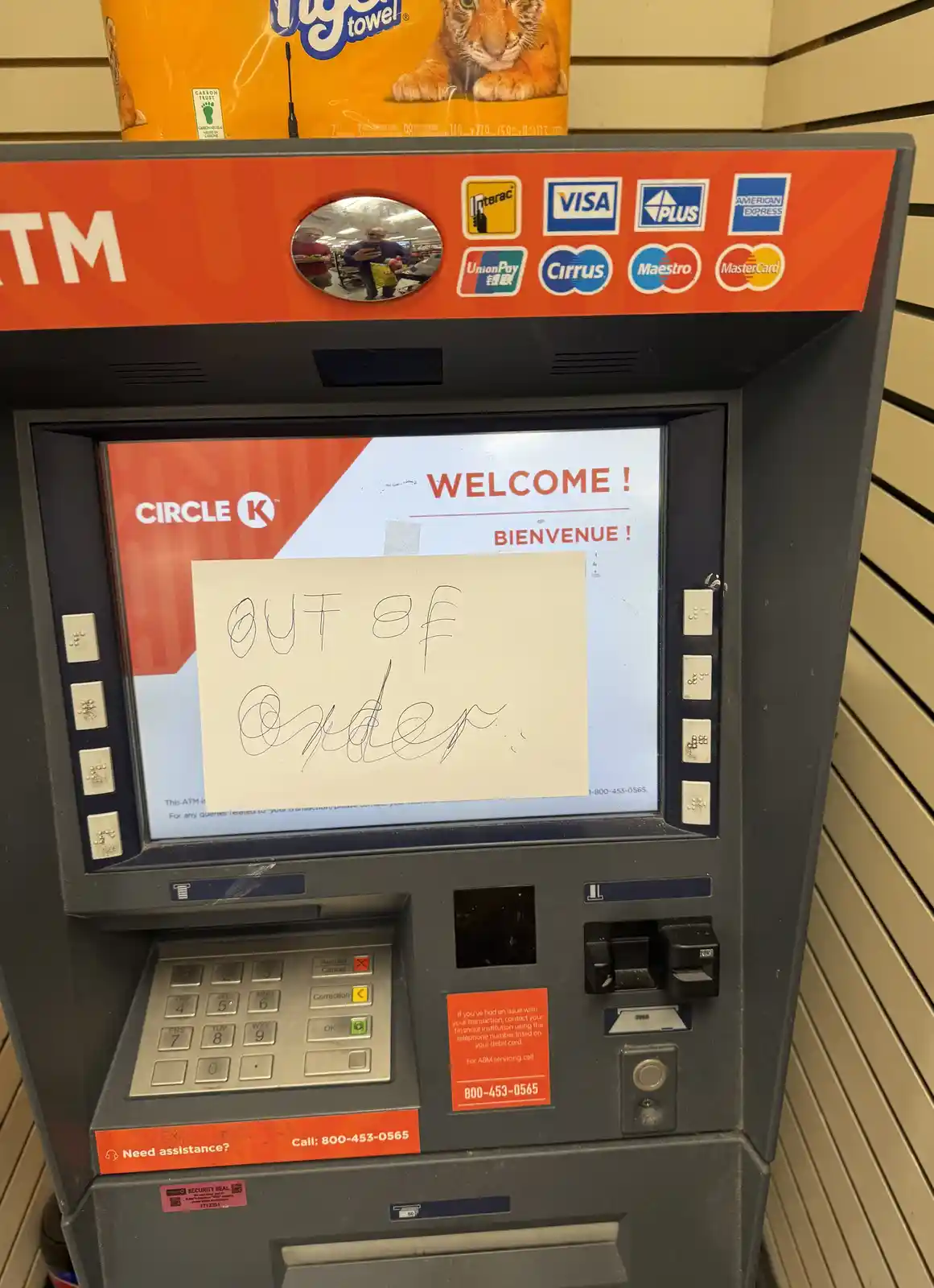 A Circle K ATM machine has a handwritten note taped over its screen that reads 'OUT OF ORDER'. The screen behind the note…