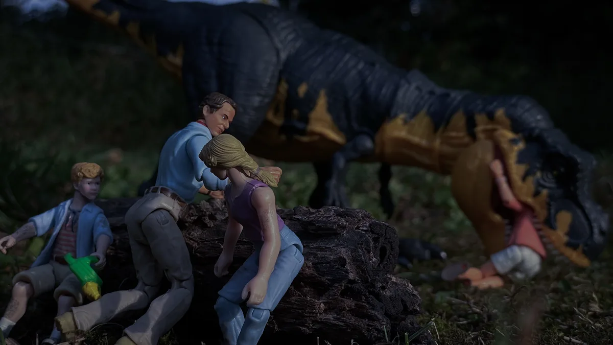 A photo of toy figurines from Jurassic Park, showing a man comforting a woman while a large t-rex toy looms behind them…